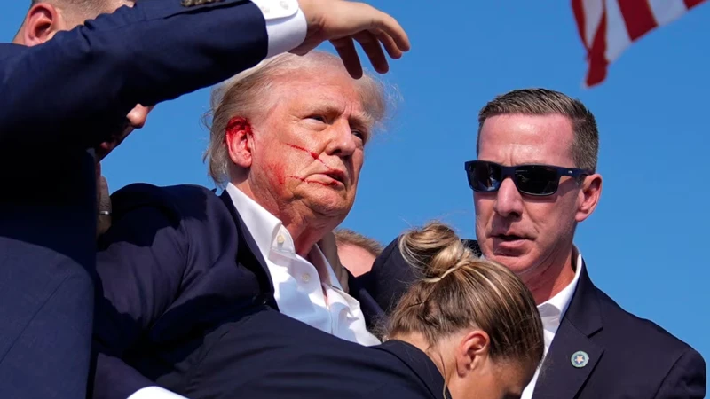 ট্রাম্পকে রক্তাক্ত অবস্থায় সিক্রেট সার্ভিস অফিসাররা ঘিরে ধরে স্টেজ থেকে নিরাপদ স্থানে সরিয়ে নিচ্ছে।